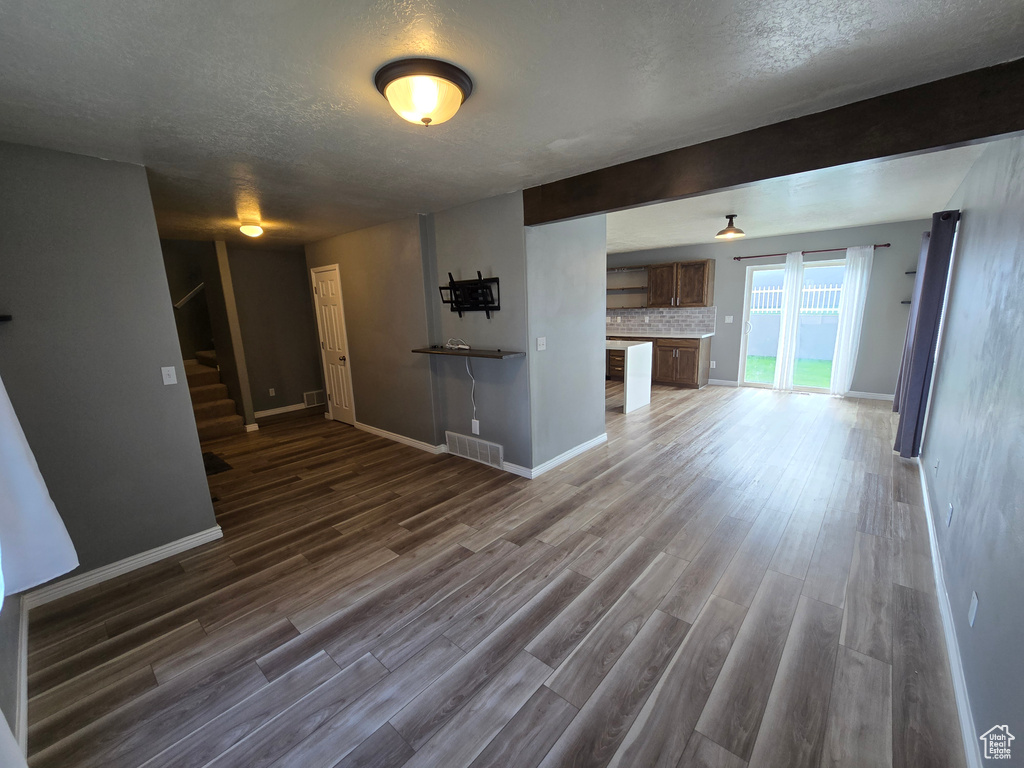 Unfurnished living room featuring a textured ceiling, stairs, baseboards, and dark wood-style floors