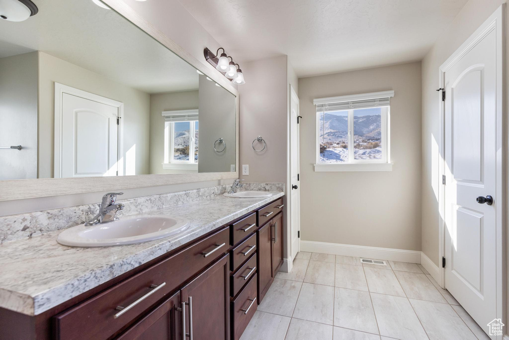 Bathroom with double vanity, plenty of natural light, baseboards, and tile patterned flooring