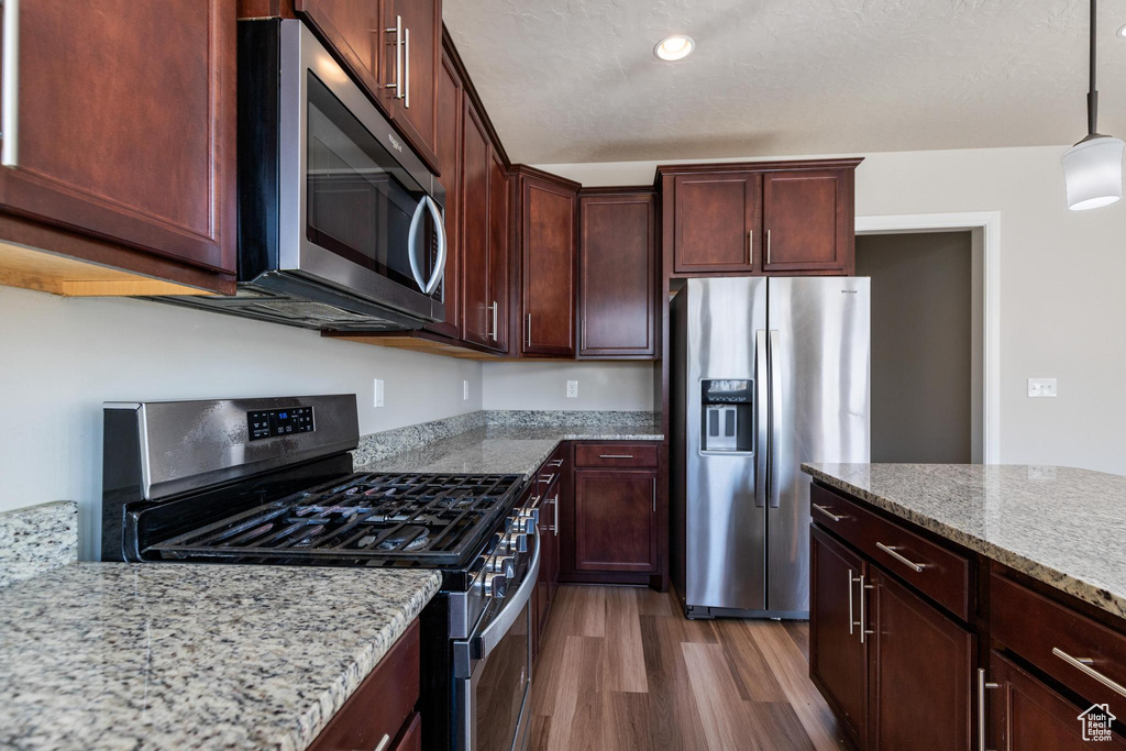 Kitchen with stainless steel appliances, dark wood-style floors, light stone countertops, and decorative light fixtures