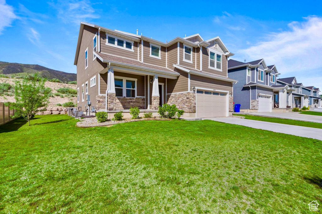 View of front facade with stone siding, an attached garage, driveway, a front yard, and a porch