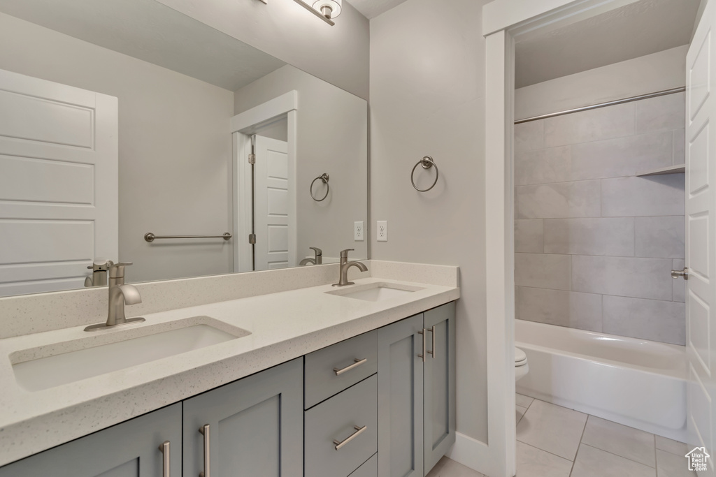 Full bathroom with toilet, double vanity, tile patterned floors, shower / tub combination, and baseboards