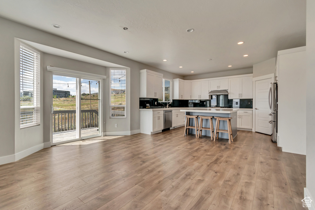 Kitchen with appliances with stainless steel finishes, a center island, under cabinet range hood, white cabinets, and recessed lighting