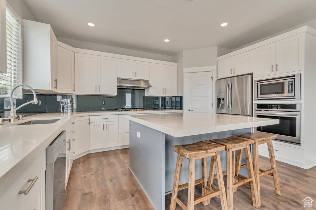 Kitchen with stainless steel appliances, a sink, a kitchen bar, light wood finished floors, and a kitchen island