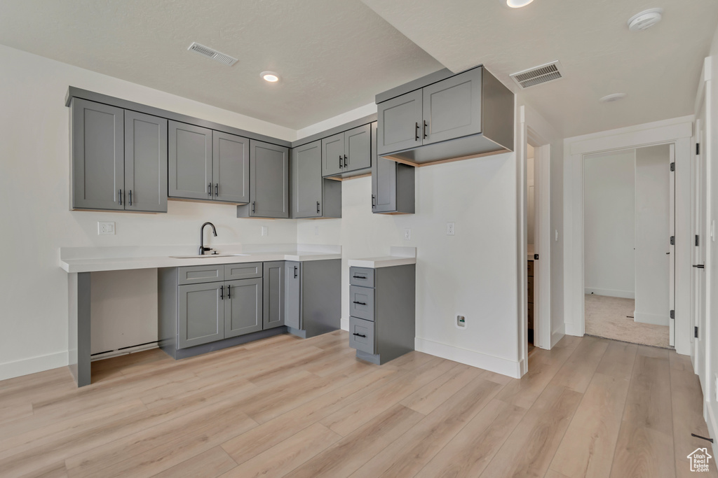 Kitchen with gray cabinets, a sink, baseboards, light wood-style floors, and recessed lighting