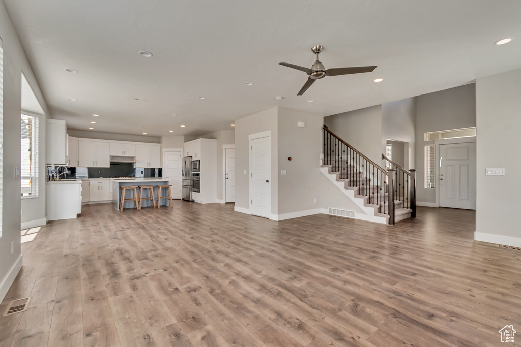 Unfurnished living room featuring stairway, ceiling fan, baseboards, recessed lighting, and light wood-style floors