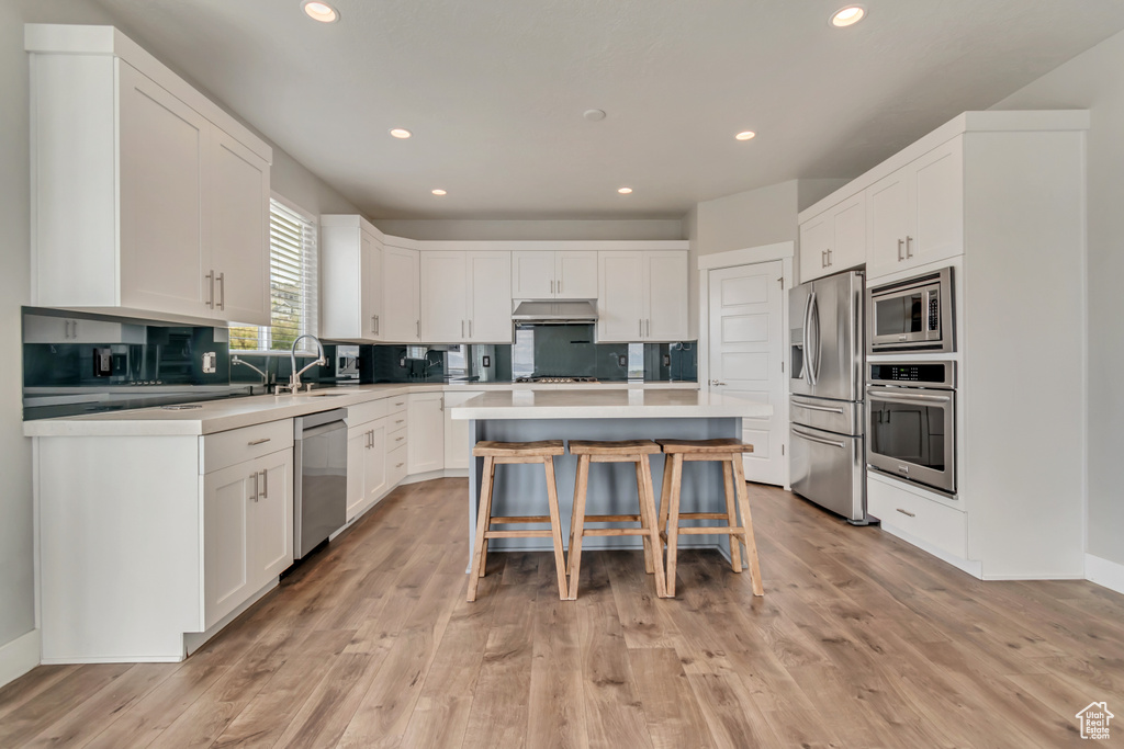Kitchen featuring stainless steel appliances, a kitchen bar, white cabinetry, recessed lighting, and tasteful backsplash