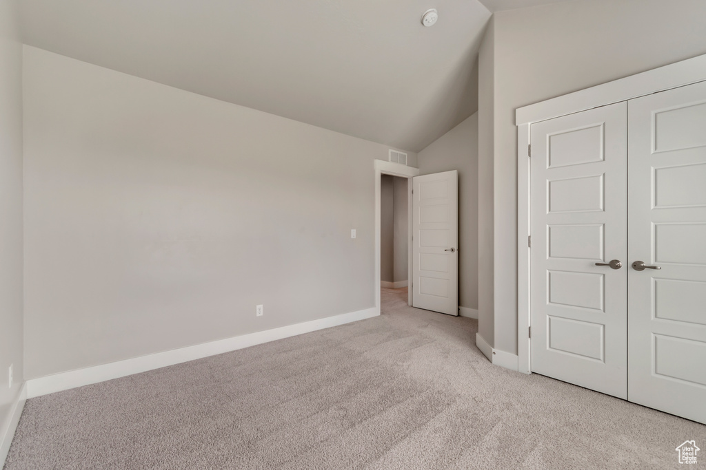 Unfurnished bedroom featuring light colored carpet, lofted ceiling, baseboards, and a closet