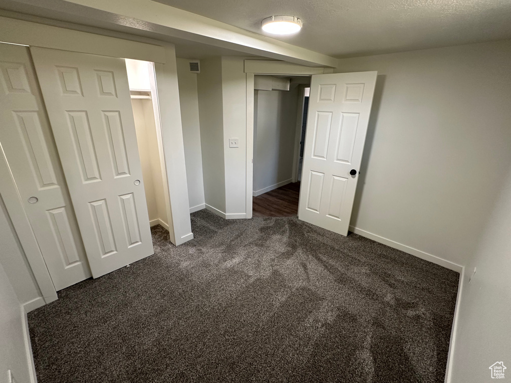 Unfurnished bedroom with dark colored carpet and baseboards
