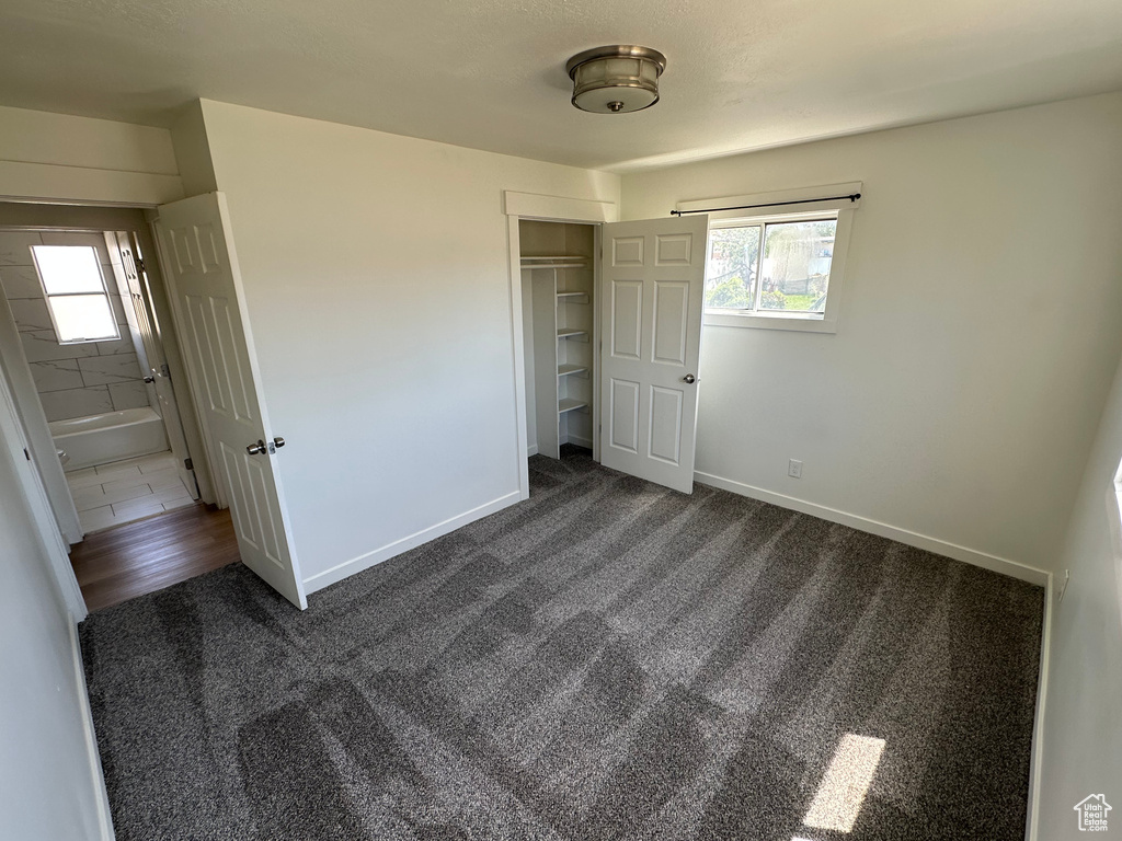 Unfurnished bedroom with dark colored carpet, multiple windows, a closet, and baseboards