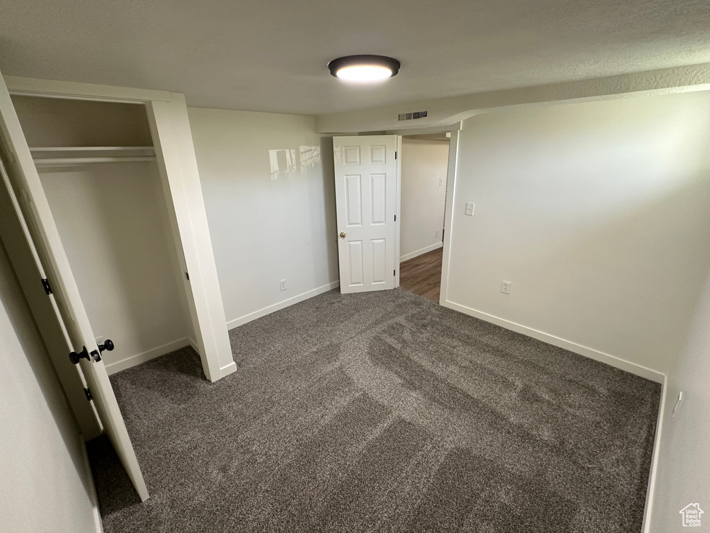 Unfurnished bedroom with dark carpet, baseboards, and a closet