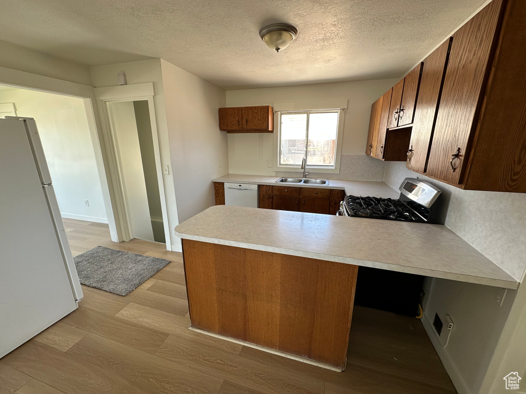 Kitchen with white appliances, a sink, a peninsula, light countertops, and light wood finished floors