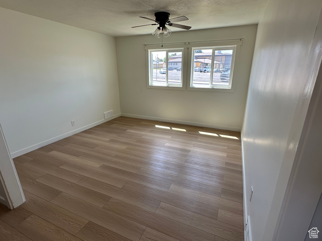 Spare room with ceiling fan, wood finished floors, baseboards, and a textured ceiling