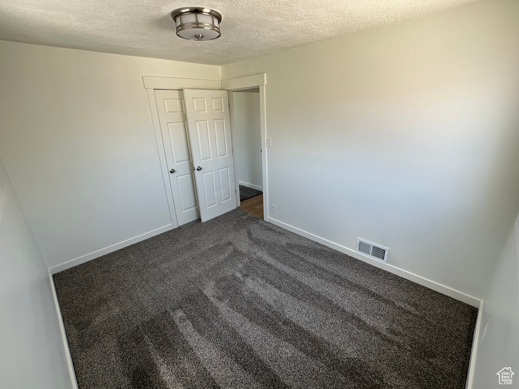 Spare room with a textured ceiling, dark carpet, and baseboards