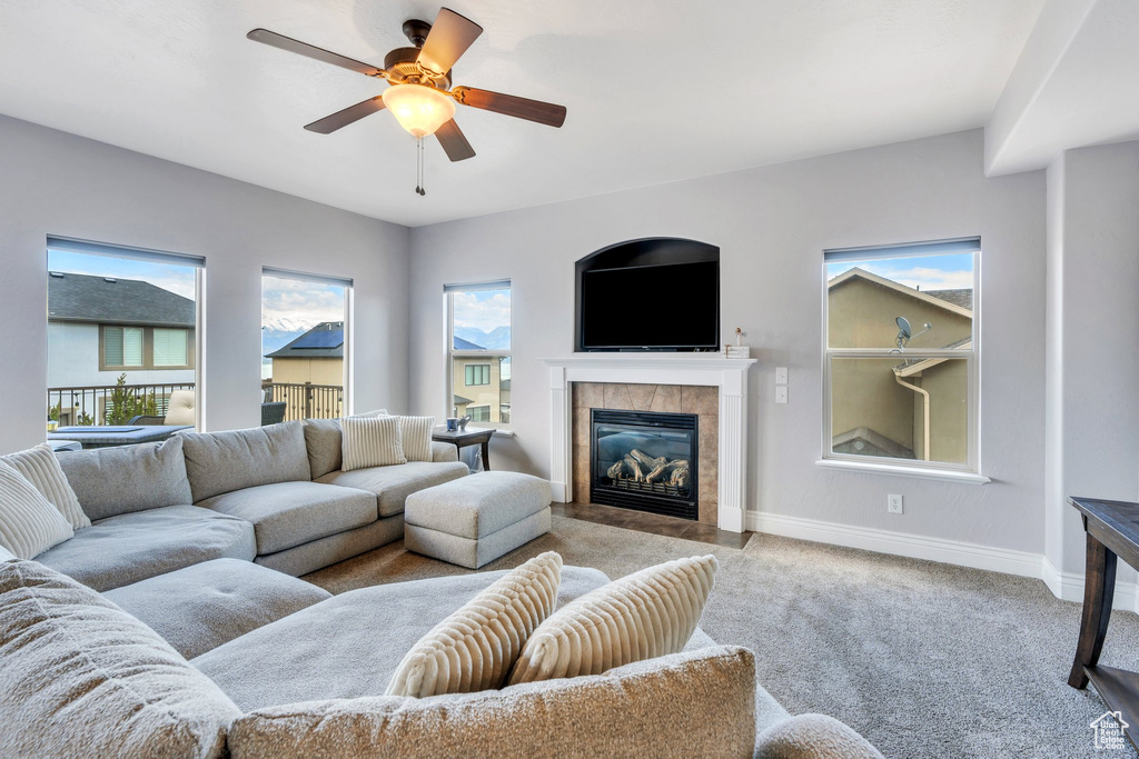 Carpeted living room featuring baseboards, a tiled fireplace, and ceiling fan