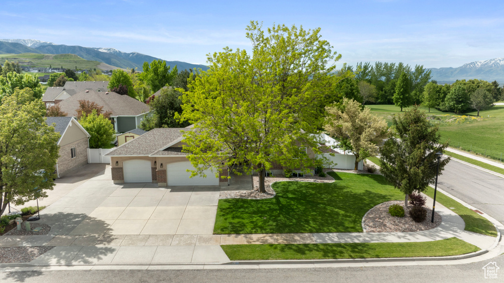View of property hidden behind natural elements featuring an attached garage, driveway, a front lawn, and a mountain view