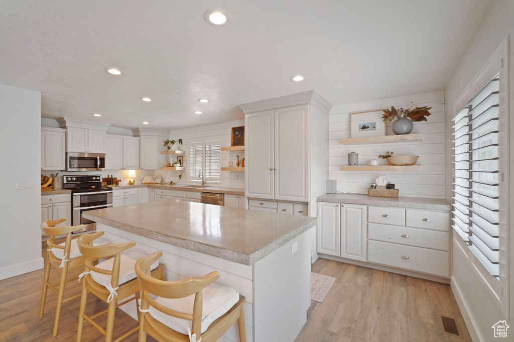 Kitchen featuring open shelves, appliances with stainless steel finishes, a sink, white cabinetry, and light wood-style flooring
