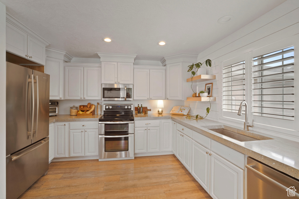 Kitchen featuring appliances with stainless steel finishes, a sink, light countertops, open shelves, and white cabinets