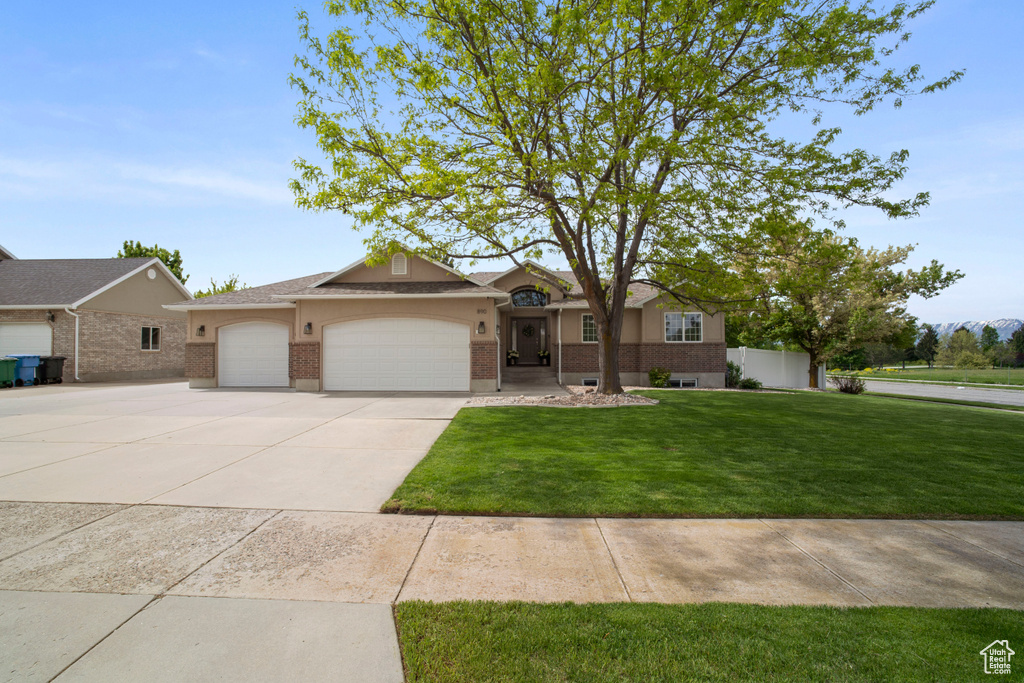 Ranch-style home featuring brick siding, a garage, a front lawn, and driveway