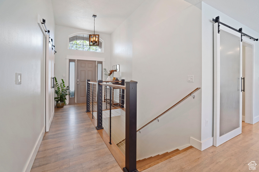 Foyer entrance featuring a barn door, light wood-type flooring, baseboards, a chandelier, and a towering ceiling