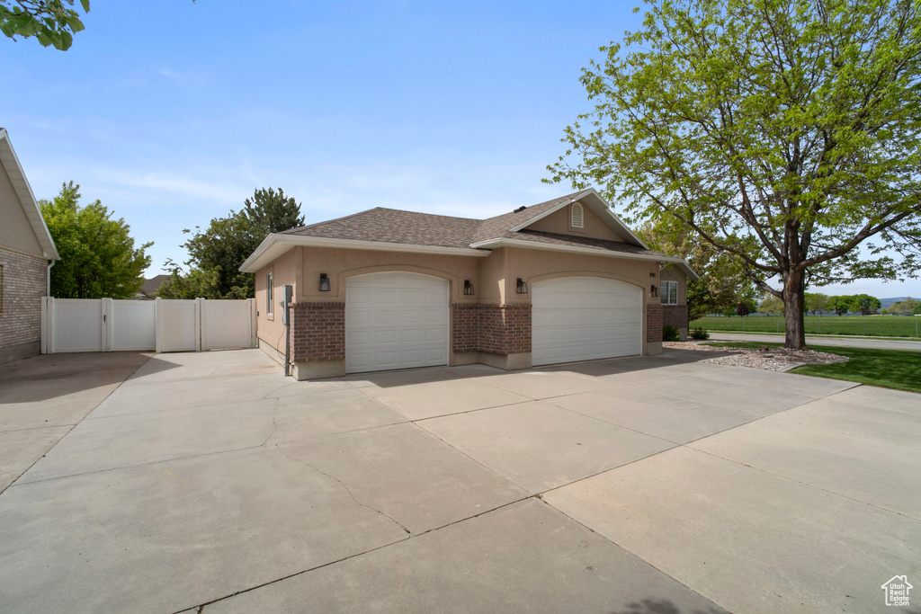View of front facade with brick siding, a garage, driveway, roof with shingles, and stucco siding