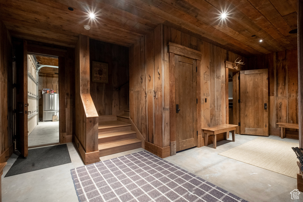 Basement with wood ceiling, wooden walls, freestanding refrigerator, and stairway