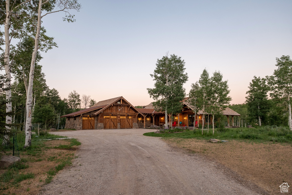 View of front of house featuring dirt driveway, stone siding, and a garage