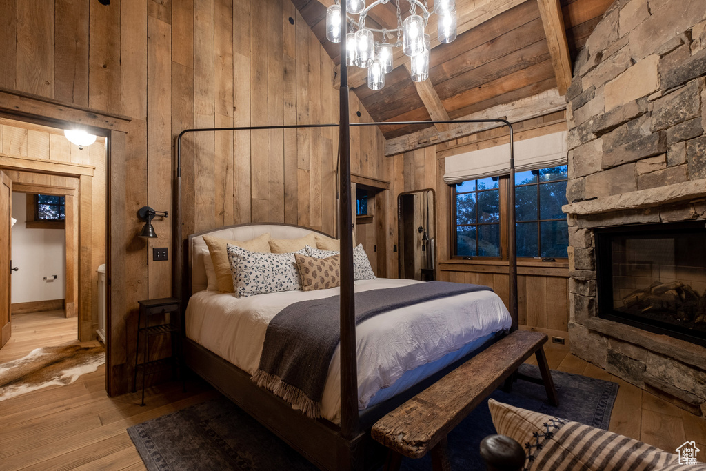 Bedroom with wood walls, high vaulted ceiling, light wood-style floors, beamed ceiling, and a stone fireplace