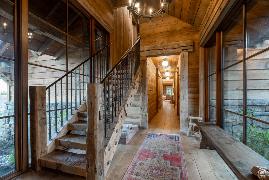 Stairway featuring wooden walls, wood-type flooring, wood ceiling, high vaulted ceiling, and a chandelier