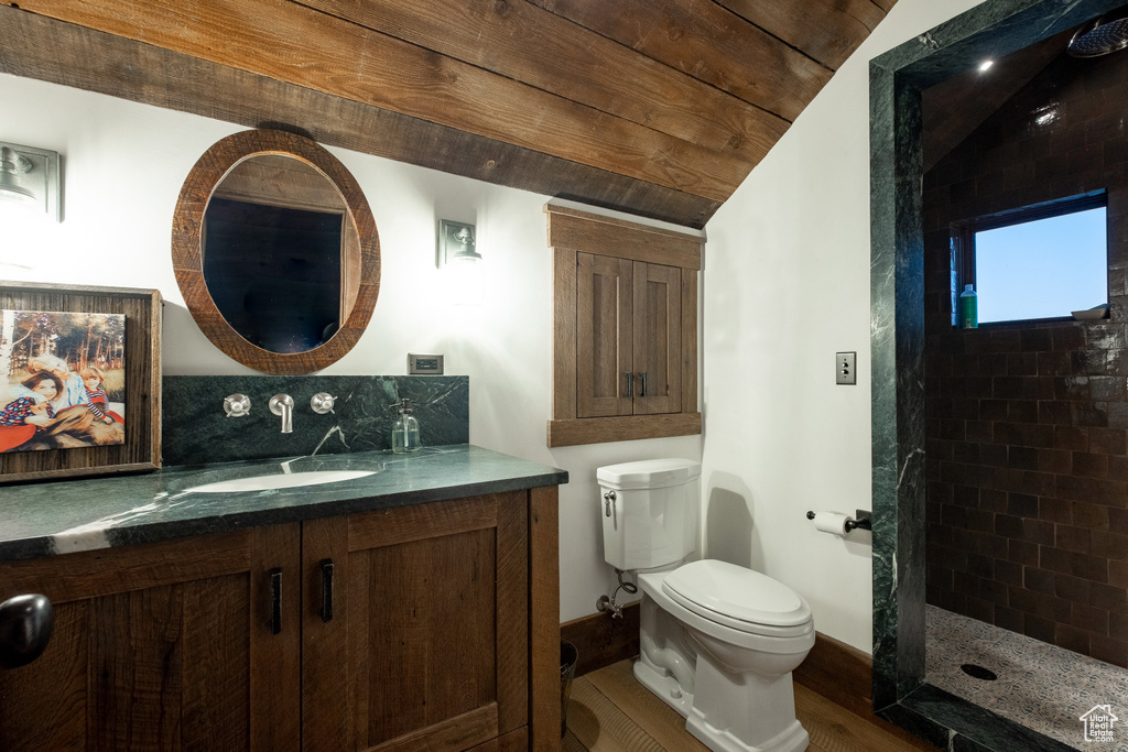 Full bath featuring toilet, tiled shower, wood finished floors, vanity, and vaulted ceiling