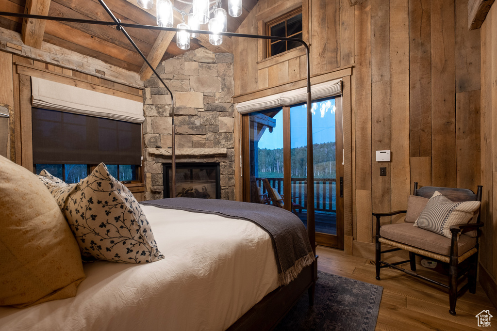 Bedroom with wooden walls, access to outside, wood finished floors, and a fireplace