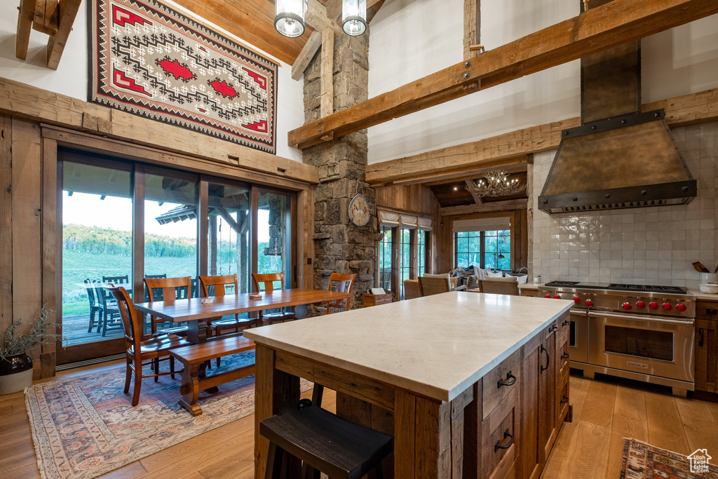 Kitchen featuring premium stove, premium range hood, a towering ceiling, light wood-type flooring, and backsplash