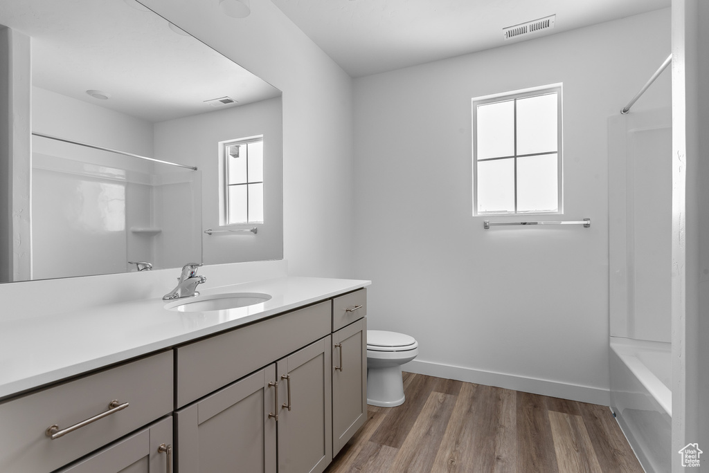 Bathroom featuring vanity, toilet, wood finished floors, shower / bath combination, and baseboards