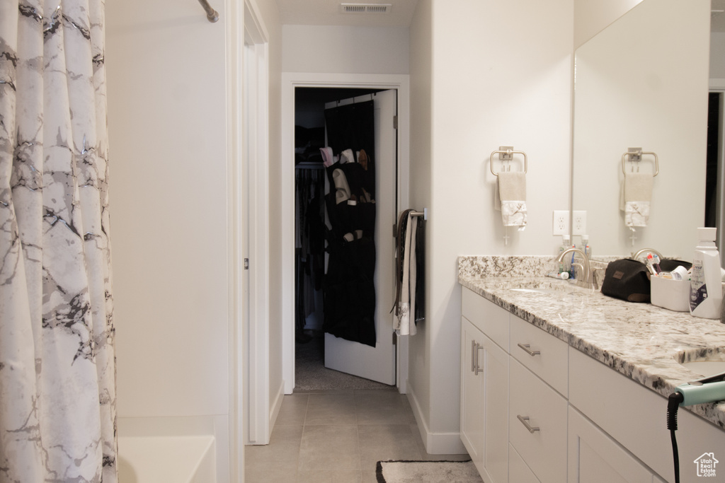 Bathroom featuring double vanity, tile patterned flooring, a walk in closet, and baseboards