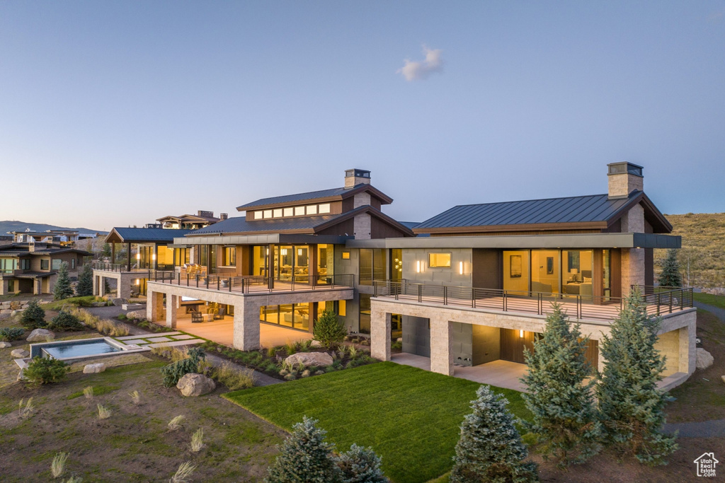 Rear view of property featuring a balcony, a chimney, a standing seam roof, and a patio area
