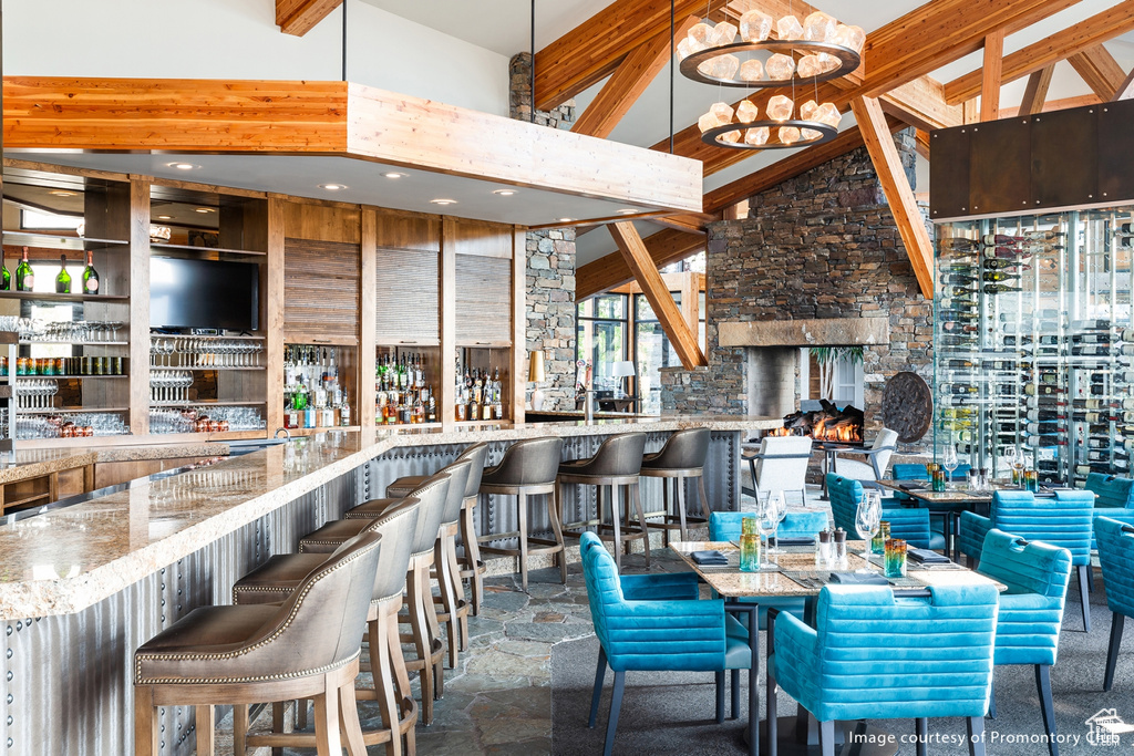 Dining area with a towering ceiling, a community bar, stone finish floors, and beamed ceiling