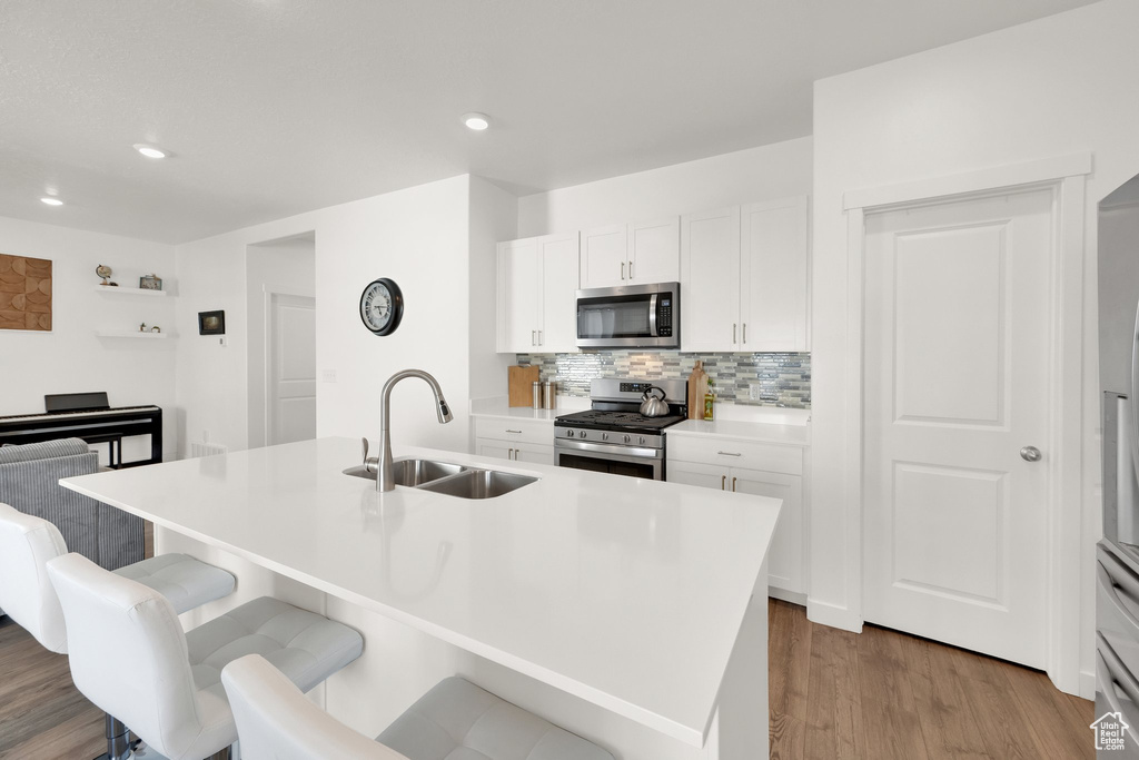 Kitchen with appliances with stainless steel finishes, a sink, a kitchen bar, white cabinetry, and recessed lighting