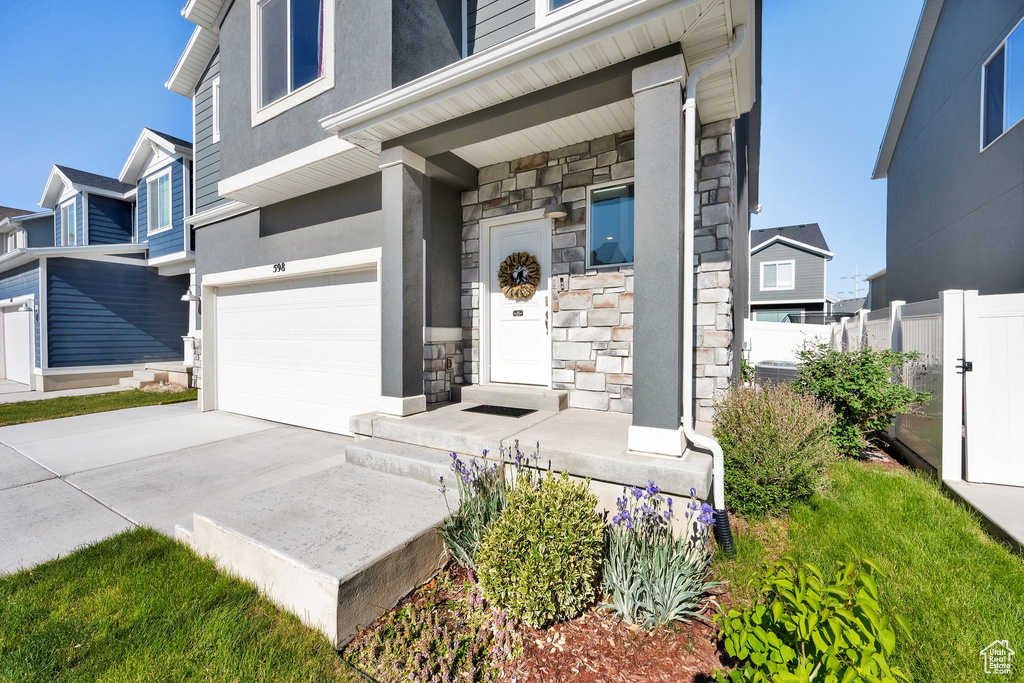 View of exterior entry with stone siding, an attached garage, driveway, and stucco siding