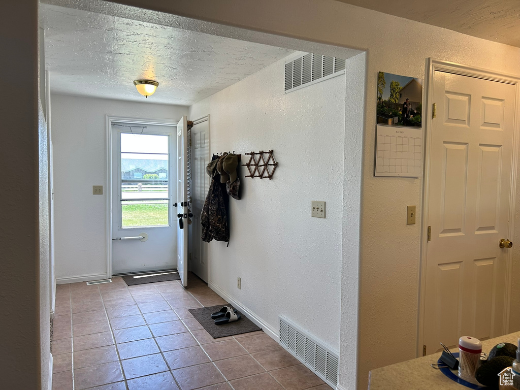 Doorway with tile patterned floors, a textured wall, a textured ceiling, and baseboards