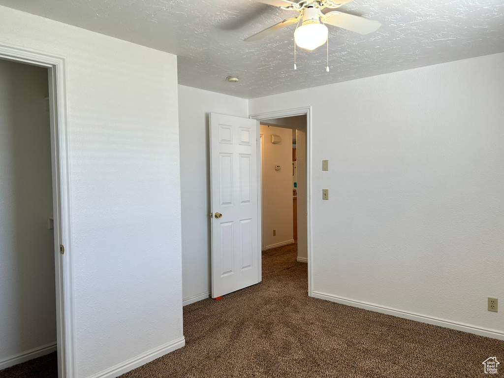 Unfurnished bedroom with dark colored carpet, baseboards, and ceiling fan