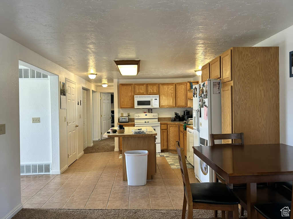 Kitchen with white appliances, a kitchen island, light tile patterned floors, baseboards, and brown cabinets