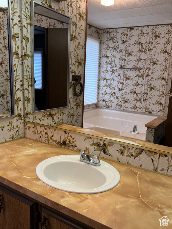 Bathroom featuring wallpapered walls, a garden tub, and vanity