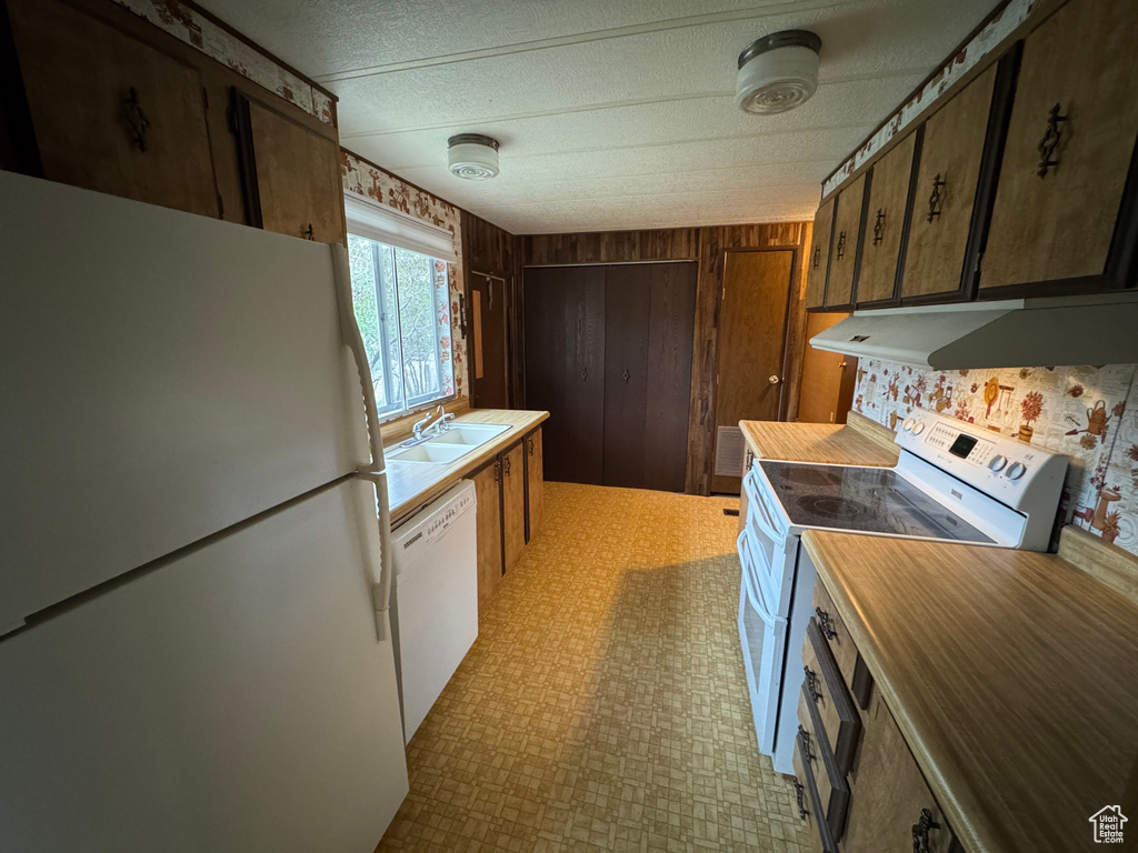 Kitchen with white appliances, a sink, under cabinet range hood, light floors, and a textured ceiling