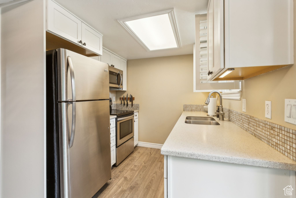 Kitchen with appliances with stainless steel finishes, a sink, white cabinets, light wood-style floors, and light stone counters