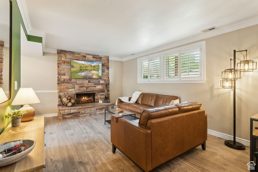 Living area featuring wood finished floors, a stone fireplace, crown molding, and baseboards