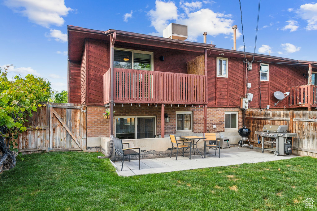 Rear view of house with a gate, a balcony, a patio, and brick siding