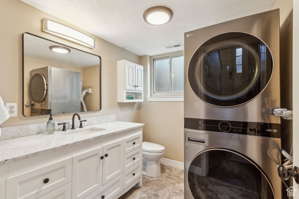 Bathroom with stacked washer and clothes dryer, toilet, vanity, and baseboards
