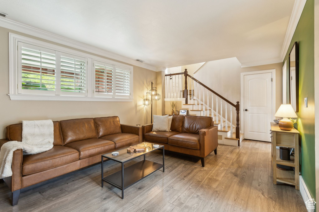 Living room featuring stairs, light wood-type flooring, and ornamental molding