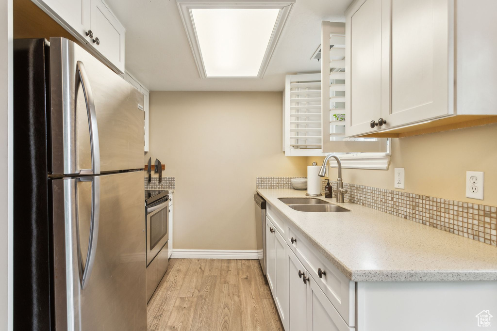 Kitchen with stainless steel appliances, a sink, light wood-type flooring, white cabinetry, and baseboards
