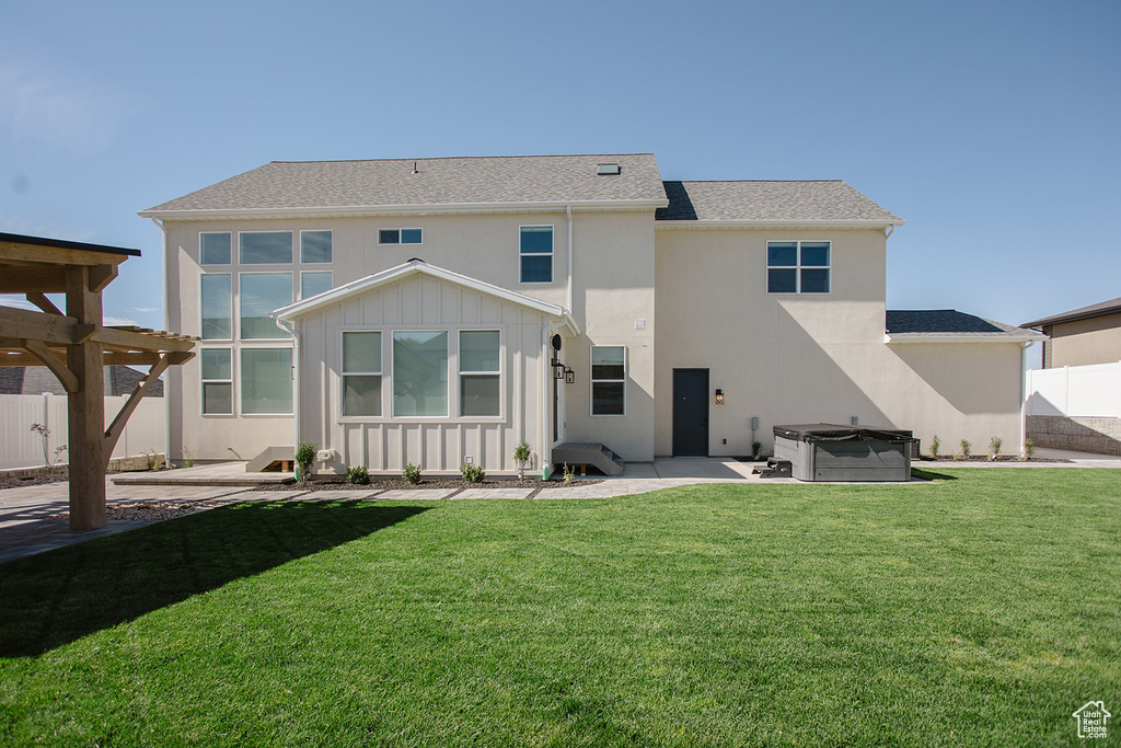 Rear view of property featuring a hot tub, a patio area, board and batten siding, and stucco siding