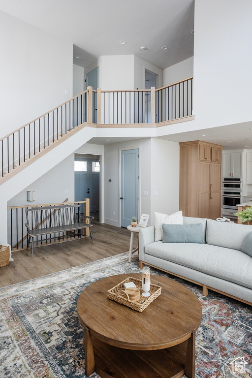 Living room with a towering ceiling, wood finished floors, stairs, and recessed lighting